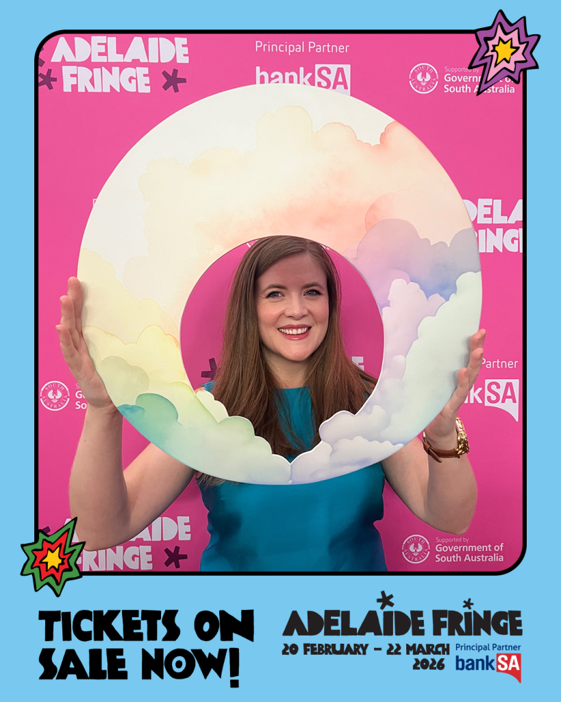 Joanne Hartstone holds her logo of rainbow clouds whilst standing against a pink Adelaide Fringe branded background.